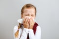 Little girl in a warm scarf blows her nose. Sick child on a gray background. Cold season