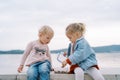 Little girl watches her friend open a lunchbox and scoop up granola with a spoon while sitting on a stone fence