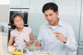 Little girl watching father eat food with a fork in kitchen