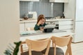 A little girl is watching a tablet attentively while sitting alone at a table and eating her quick breakfast with a