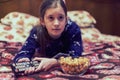 Little girl is watching tv and eating popcorn in her bed. Little girl watching tv. Teen girl eating popcorn in front of the TV. Royalty Free Stock Photo