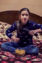 Little girl is watching tv and eating popcorn in her bed. Little girl watching tv. Teen girl eating popcorn in front of the TV. Royalty Free Stock Photo