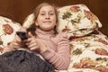Little girl watching TV lying on bed with remote control in hand. toned Royalty Free Stock Photo