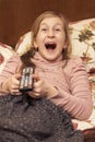 Little girl watching TV lying on bed with remote control in hand. vertical photo. toned Royalty Free Stock Photo