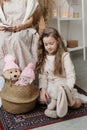 A little girl with wavy hair is cute playing with toys, and her mother is sitting in a chair