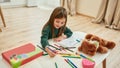 A little girl sitting alone at the table and painting with pencils in a huge bright room smiling and enjoying drawing Royalty Free Stock Photo