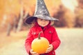 Little girl wearing Halloween witch hat and warm red coat, having fun in autumn day.