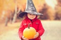 Little girl wearing Halloween witch hat and warm red coat, having fun in autumn day. Royalty Free Stock Photo