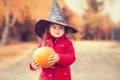 Little girl wearing Halloween witch hat and warm red coat, having fun in autumn day. Royalty Free Stock Photo