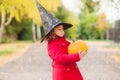 Little girl wearing Halloween witch hat and warm red coat, having fun in autumn day. Royalty Free Stock Photo