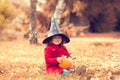 Little girl wearing Halloween witch hat and warm red coat, having fun in autumn day.