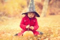 Little girl wearing Halloween witch hat and warm red coat, having fun in autumn day. Royalty Free Stock Photo