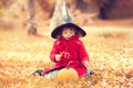 Little girl wearing Halloween witch hat and warm red coat, having fun in autumn day. Royalty Free Stock Photo