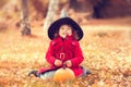 Little girl wearing Halloween witch hat and warm red coat, having fun in autumn day. Royalty Free Stock Photo