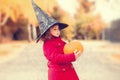 Little girl wearing Halloween witch hat and warm red coat, having fun in autumn day. Royalty Free Stock Photo