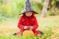 Little girl wearing Halloween witch hat and warm red coat, having fun in the park, autumn day. Royalty Free Stock Photo