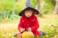 Little girl wearing Halloween witch hat and warm red coat, having fun in the park, autumn day. Royalty Free Stock Photo