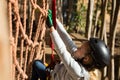 Little girl wearing helmet climbing on rope fence in the forest Royalty Free Stock Photo