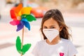 Little girl wearing mask and holding a colorful toy windmill, or pinwheel. Royalty Free Stock Photo