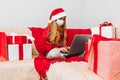 Little girl wearing medical mask  santa claus hat while talking to online friend on laptop while sitting on sofa at home for Royalty Free Stock Photo