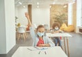 Little girl wearing protective face mask during coronavirus outbreak raised her hand in class. School child studying in Royalty Free Stock Photo