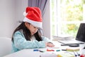 The little girl is wearing a red Santa hat, sitting and coloring. Royalty Free Stock Photo