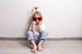 a little girl wearing sunglasses is sitting on the floor of a room against the wall. Royalty Free Stock Photo