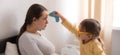 little girl wearing uniform playing doctor, nurse with young mum, nanny in bedroom, checking mother throat, measures Royalty Free Stock Photo