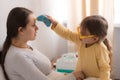 little girl wearing uniform playing doctor, nurse with young mum, nanny in bedroom, checking mother throat, measures Royalty Free Stock Photo