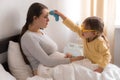 little girl wearing uniform playing doctor, nurse with young mum, nanny in bedroom, checking mother throat, measures Royalty Free Stock Photo