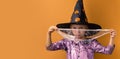 Little girl wearing violet Halloween dress and witch hat covered with spider net with black spooky spiders on it. Orange