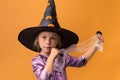 Little girl wearing violet Halloween dress and witch hat covered with spider net with black spooky spiders on it. Orange