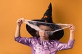 Little girl wearing violet Halloween dress and witch hat covered with spider net with black spooky spiders on it. Orange