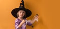 Little girl wearing violet Halloween dress and witch hat covered with spider net with black spooky spiders on it. Orange