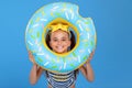 Little girl wears striped swimwear and goggles on her head, looking through inflatable swim ring