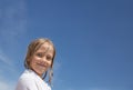 A little girl with wet blond hair, wrapped in a white towel, smiles against the blue sky. Summer vacation at sea. Happy Holidays Royalty Free Stock Photo