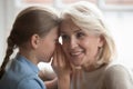 Little girl whisper in ear tell secret to curious grandmother