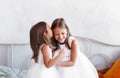 Little girl whispers in her sister`s ear. Two girls girlfriends in a light room Royalty Free Stock Photo