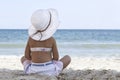 Little girl in a white beach hat and bikini sits on the sand by the sea Royalty Free Stock Photo