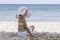 Little girl in a white beach hat and bikini sits on the sand by the sea Royalty Free Stock Photo