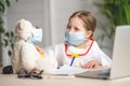 Little girl in a white coat and mask, using stethoscope, listens to Teddy bears Royalty Free Stock Photo