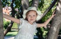 Little girl in a white dress and panama sits on a tree