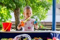 A little girl in a white dress shyly catches a toy, playing fishing in a children`s pool Royalty Free Stock Photo