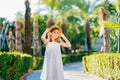 little girl in a white dress and a straw hat on the path in a tropical hotel