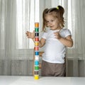 Little girl in a white foot-shirt stands on a chair with builds a turret of colored jars