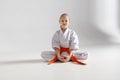 A little girl in a white kimono sits on a light background, karate Royalty Free Stock Photo