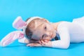 Little girl in a white rabbit costume on a blue background. The baby lies dreaming on the floor. Royalty Free Stock Photo