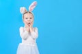 Little girl in a white rabbit costume. Surprised baby. Cute bunny, holiday symbol. Bright photo on a blue background. Royalty Free Stock Photo