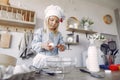 Little girl in a white shef hat cook the dough for cookies