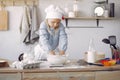 Little girl in a white shef hat cook the dough for cookies